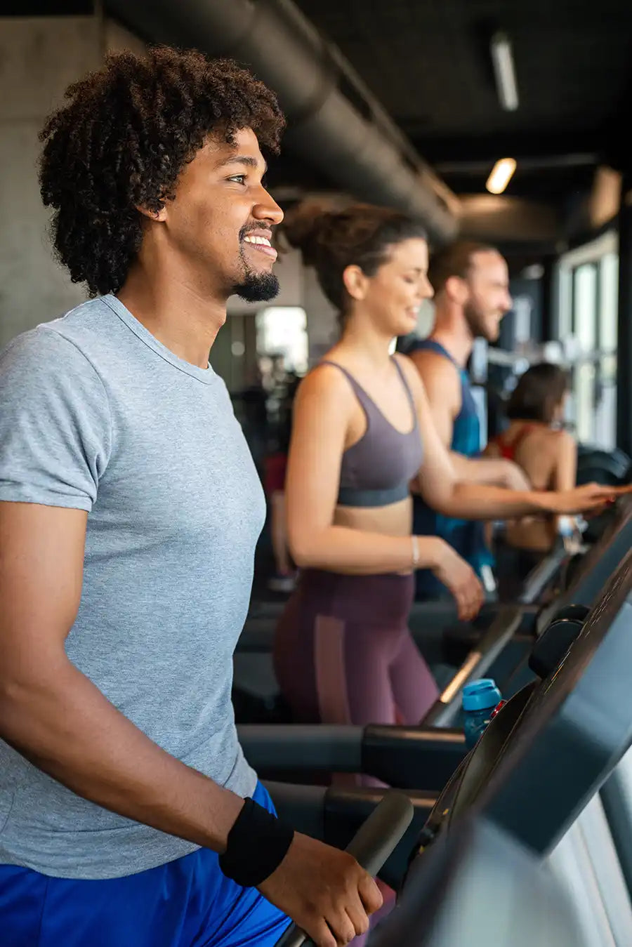 Man using a treadmill in a gym with other people in the background